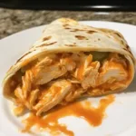Close-up of a Buffalo Chicken Wrap filled with spicy chicken, crisp lettuce, shredded cheese, and creamy ranch dressing in a soft tortilla.